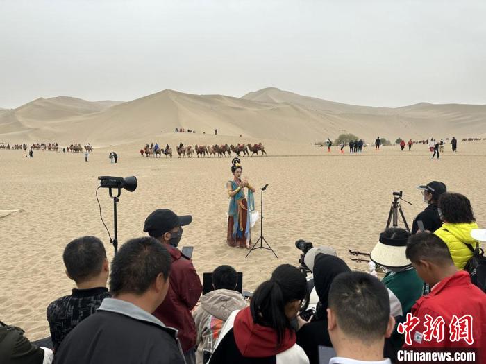 圖為2023年4月底，敦煌大漠“逐舞者”奧楠在鳴沙山月牙泉景區(qū)視頻直播，吸引游人圍觀?！●T志軍 攝